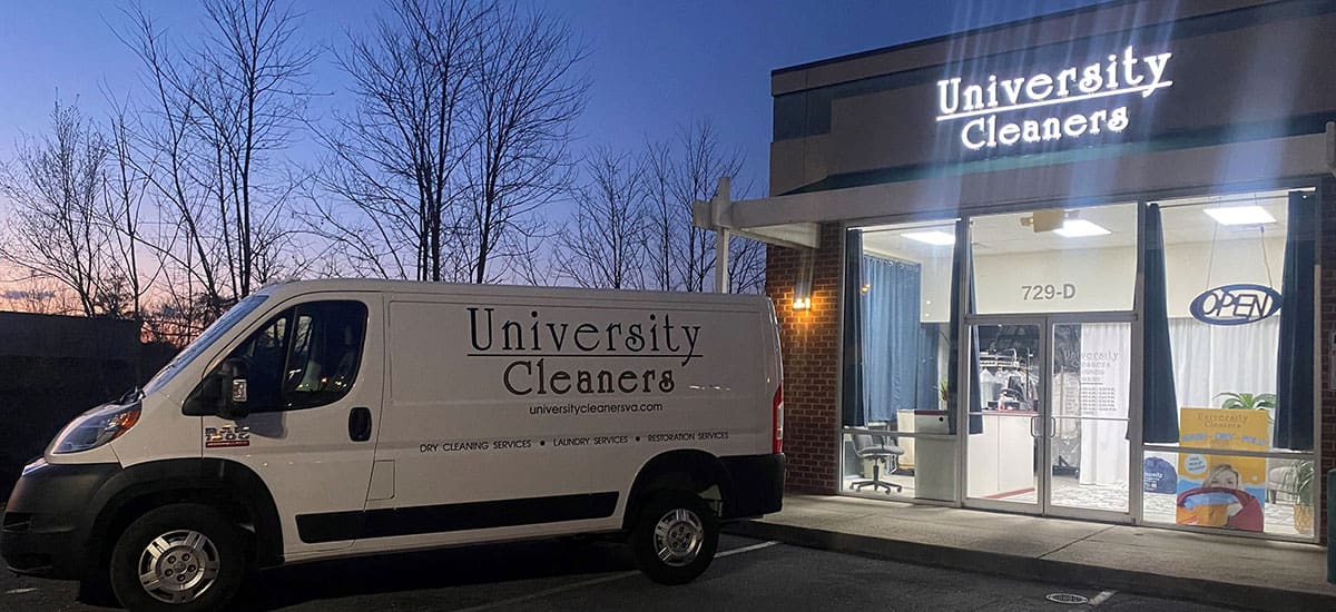 A University Cleaners van is parked outside the University Cleaners storefront at dusk, with lights on inside and an open sign displayed.
