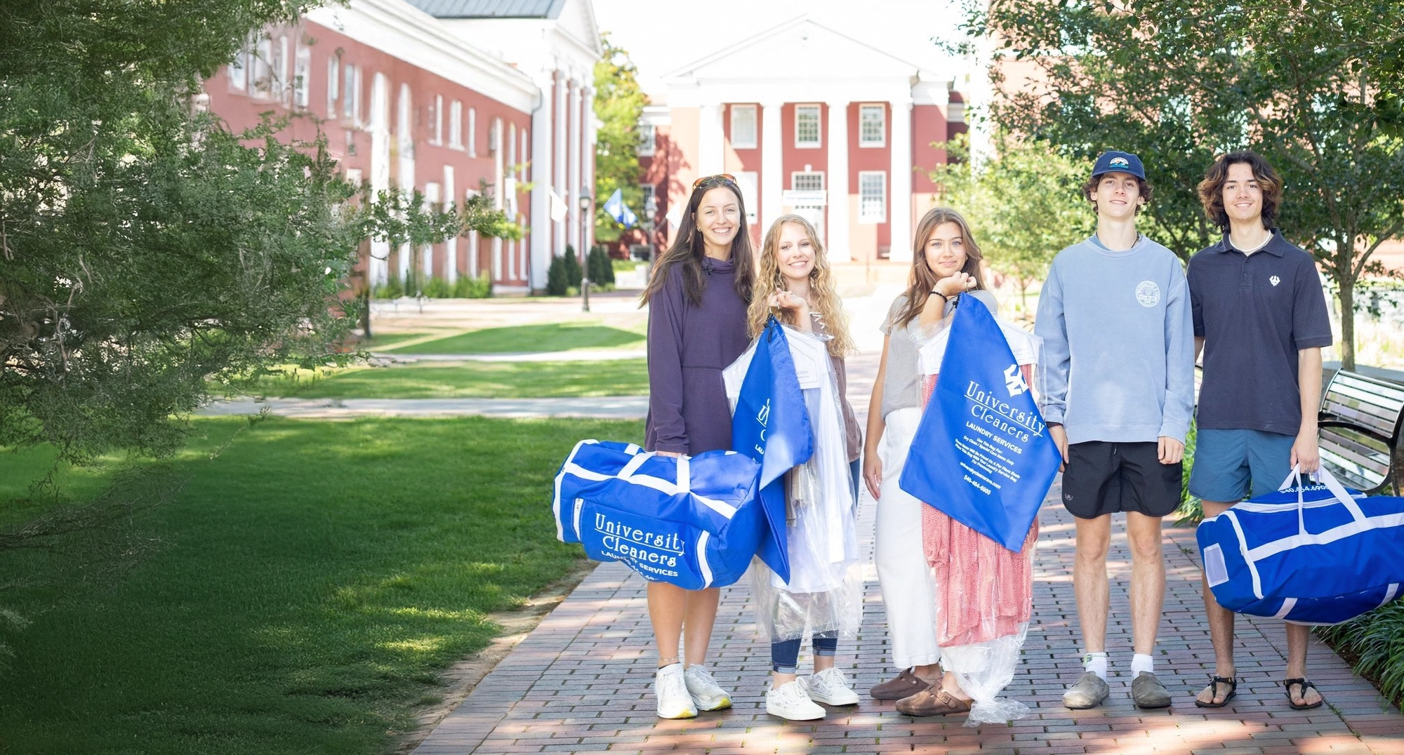 Five young people stand on a brick walkway holding blue bags labeled 