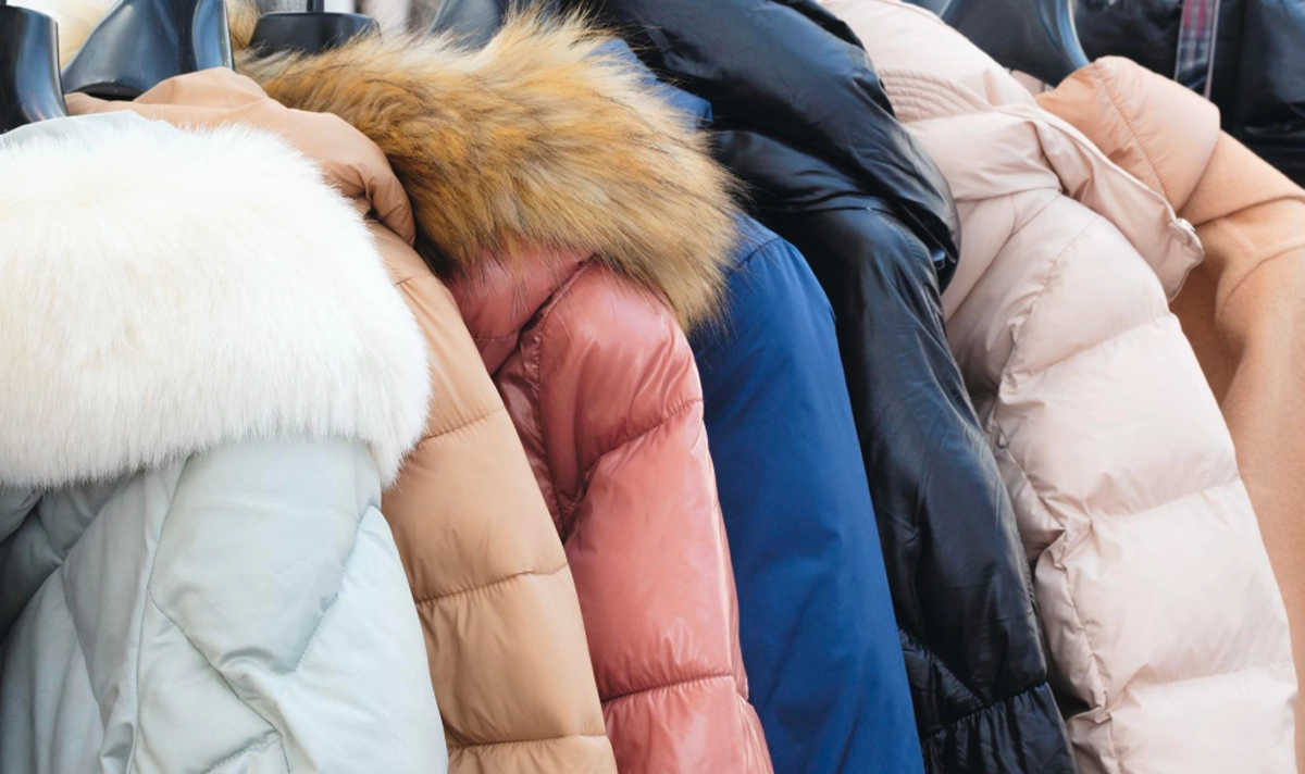 A row of winter jackets in various colors and styles, including some with fur-trimmed hoods, hanging on display.