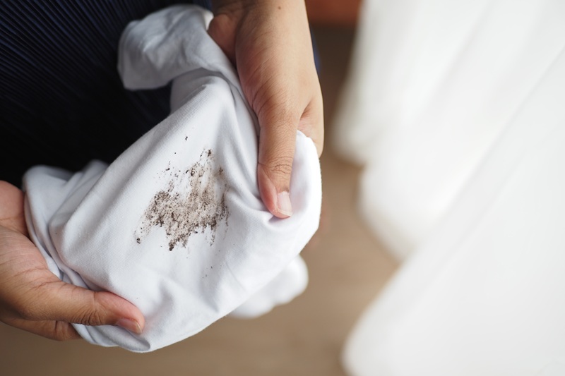 Close-up of hands holding a white shirt with a visible dirt stain.