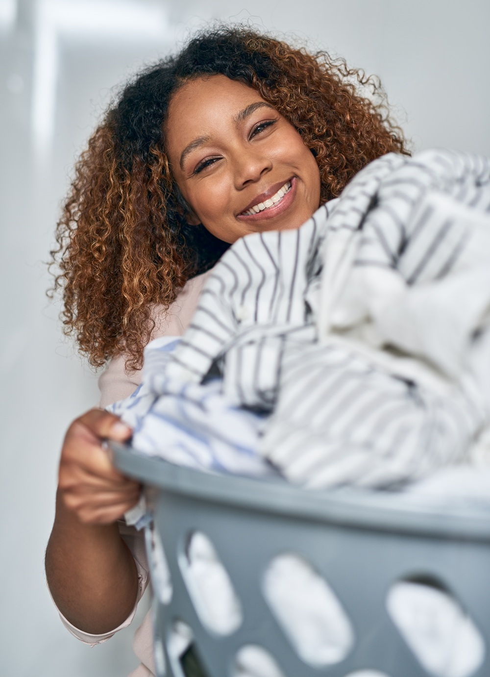 Young woman smiling while holding a laundry basket filled with clothes.